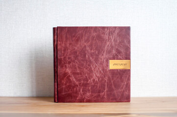 A handmade photobook made of old brown leather with engraving lies on a wooden table on a solid...