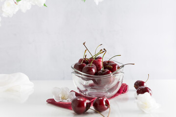 Cerezas en un recipiente de vidrio con una rama de cerezo en flor sobre fondo blanco