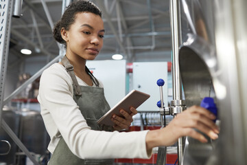 Portrait of young African-American woman operating brewing equipment at beer making factory and using digital tablet, copy space - Powered by Adobe