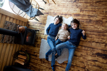 Three sweet children, siblings lying on the floor in little fancy wooden cottage, reading a book, drinking tea