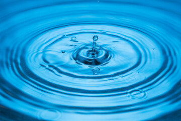 Close up view of Drops making circles on blue water surface isolated on background.