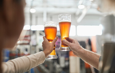 Close up of two workers holding beer glasses while inspecting quality of production and filtration...