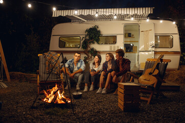 Friends sitting by campfire in the night, camping - obrazy, fototapety, plakaty