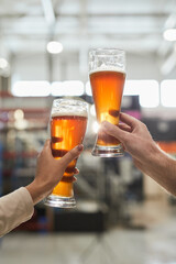 Vertical close up of two workers holding beer glasses while inspecting quality of production and...