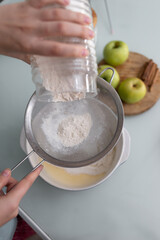 Close-up of a girl in the kitchen pours and sows flour through a metal sieve into a ceramic bowl for beating. Home baking concept. The process of making pie.