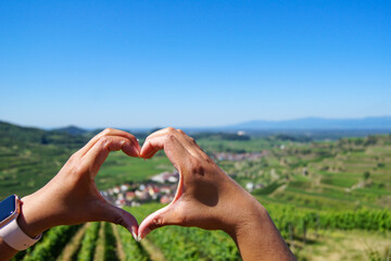 Close-up of a woman's hands forming a heart around a beautiful village surrounded by vineyards at...