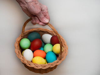 Old, elderly woman holds in her hand a multicolored, painted boiled chicken eggs in a wicker wooden, rustic basket. Traditional elements of a happy Orthodox or Catholic Easter.