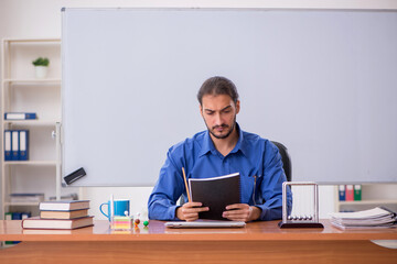 Young male teacher physicist sitting in the classroom