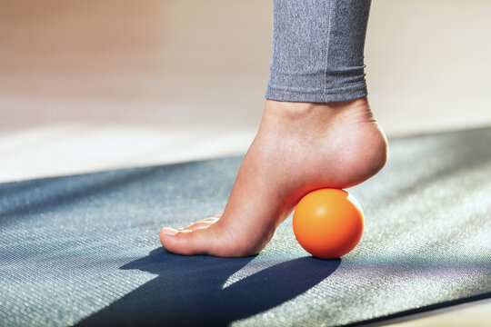Myofascial release of hyper-movable muscles of the foot with a massage ball on a gymnastic mat at home. Prevention of leg fatigue after wearing high heel shoes - Powered by Adobe