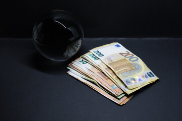 crystal ball lies behind a stack of money with euro banknotes