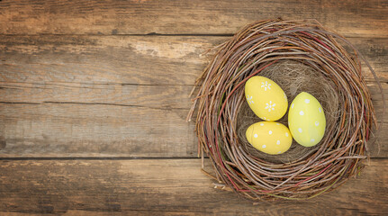 Three yellow Easter eggs in bird's nest on wooden background - top view	