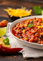 Chilli con Carne with tortilla chips and cheese in white bowl. Mexican food.