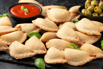 Margarita Margherita pizza parcels pockets filled with tomato, mozzarella cheese and basil served on black slate board with marinara sauce and olives. Party finger food