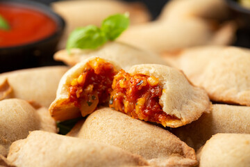 Margarita Margherita pizza parcels pockets filled with tomato, mozzarella cheese and basil served on black slate board with marinara sauce and olives. Party finger food