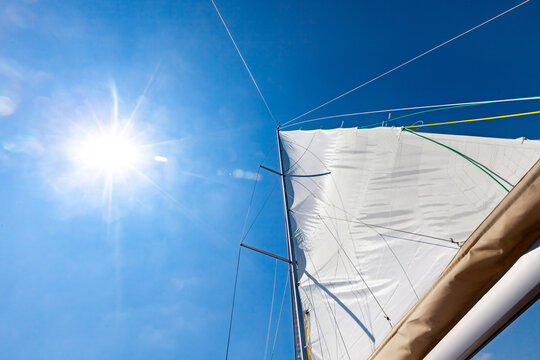 White sail against blue sky and sun