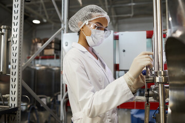 Side view portrait of young female worker wearing protective clothing while operating equipment at chemical plant, copy space