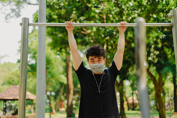 Social distancing. Young asian man in protective masks working out in park outdoors. Doing push-up and pull-up exercises. Sport in quarantine. Covid-19. Protection.