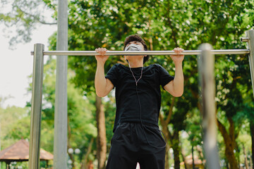 Fototapeta premium Social distancing. Young asian man in protective masks working out in park outdoors. Doing push-up and pull-up exercises. Sport in quarantine. Covid-19. Protection.
