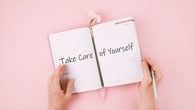 Self Care, Take care of yourself, wellbeing routine, self-care activities concept with open notebook, flower narcissus and female hand on pink background