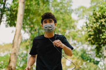 Naklejka premium Sporty young asian man wearing face mask while jogging in park.