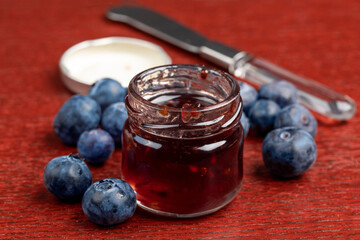 a personal or restaurant serving size jar of blueberry jelly surrounded by fresh blueberries