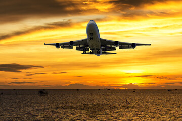 Fototapeta na wymiar front image commercial passenger aircraft or cargo transportation airplane fly over coast of sea and spread the wheel prepare landing to airport in evening with sun and golden sunset seascape view