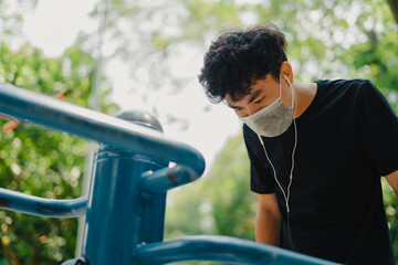 Social distancing. Young asian man in protective masks working out in park outdoors. Doing push-up and pull-up exercises. Sport in quarantine. Covid-19. Protection.