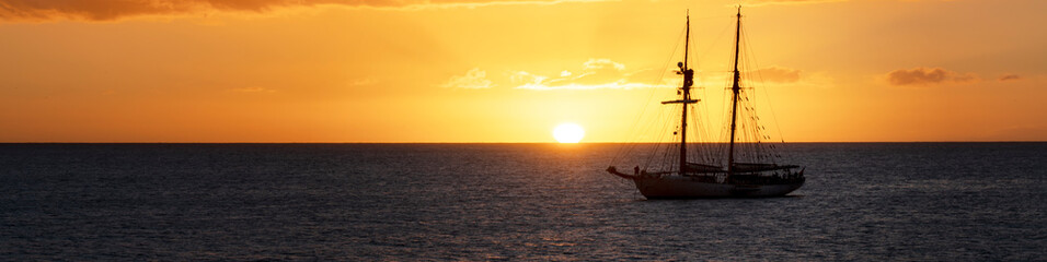 sunset on the sea with sailing ship moored offshore. Horizontal banner