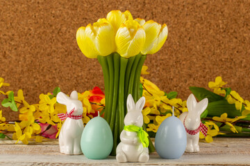 A tulip-shaped candle with Easter eggs, Easter bunnies and a bouquet of flowers on a brown background.