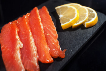 pieces of salted salmon lemon slice on a black shale stand on a black background