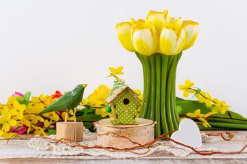 A spring arrangement of flowers with a tulip-shaped candle, a wooden bird and a birdhouse.