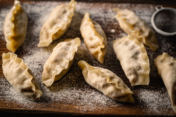 Fototapeta premium Asian raw dumplings on on wooden cutting board. Traditional chinese dim sum dumplings.