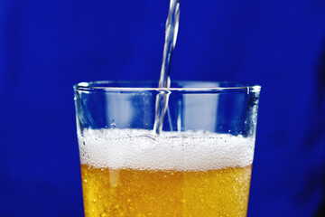 jet beer into a glass of foam bubbles close-up on a blue background