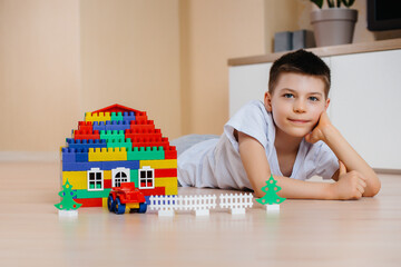 A little boy plays with a construction kit and builds a big house for the whole family. Construction of a family home.