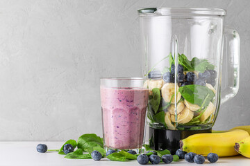 Glass of blueberry, banana and spinach smoothie with fresh juicy ingredients in blender for making healthy drink