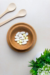 A handful of pills in a wooden plate. Surrounded by wooden spoons and a green plant. The concept of medcine, treatment. Top view, vertical photo