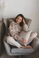 Woman dressed in comfy loungewear of grey color sitting in a cozy and comfortable armchair. Casual outfit. Home clothing. Female's portrait - 418770191