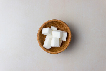 Sugar cubes in a wooden plates in center of the kitchen table. Top view