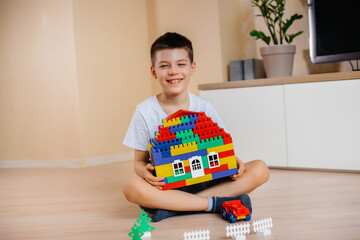 A little boy plays with a construction kit and builds a big house for the whole family. Construction of a family home.