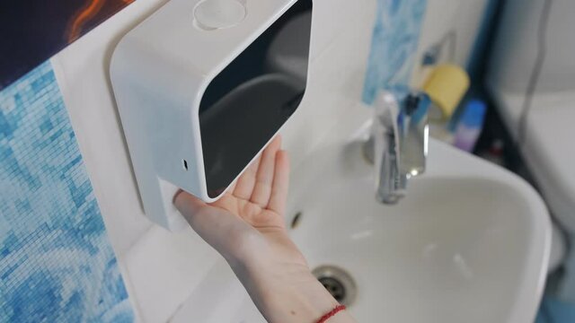 Automatic soap dispenser in the bathroom. Close-up of young teenage gerls hands using soap foam.