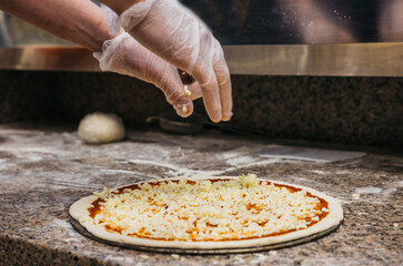 Chef with gloves sprinkles pizza with grated cheese