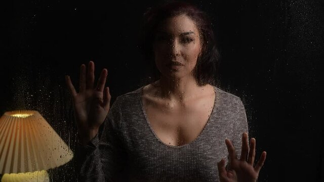 Latina woman look straight out of rainy window on a thunderous night. Looking worried and longing