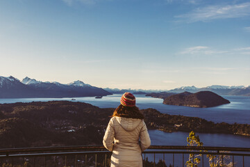 Mujer con ropa de invierno observado un paisaje de lagos y montañas