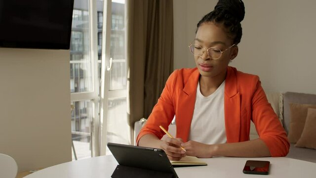 African american young bright student on a distant lecture noting down the lesson on a video call using tablet computer e-learning