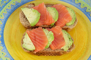 Homemade toast sandwich with salmon and avocado on a slice of cereal bread. The toast lies on a bright yellow plate. healthy food