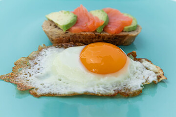 Homemade toast sandwich with salmon and avocado on a slice of cereal bread. Fried eggs with bright yolk on a mint background.