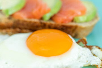 Homemade toast sandwich with salmon and avocado on a slice of cereal bread. Fried eggs with bright yolk on a mint background.