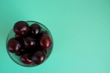 red juicy cherry in a clear glass cup on a turquoise background top view . ripe summer berries