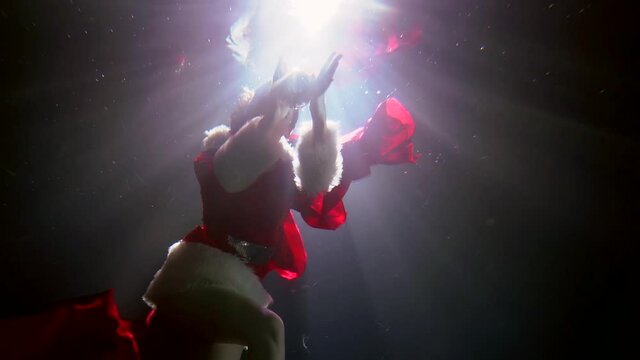 fairytale and sorcery shot underwater, woman dressed like Santa is floating in pool, playing with magic ball