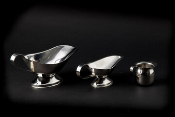 a collection of stainless steel tableware, gravy boats and creamer, isolated on black